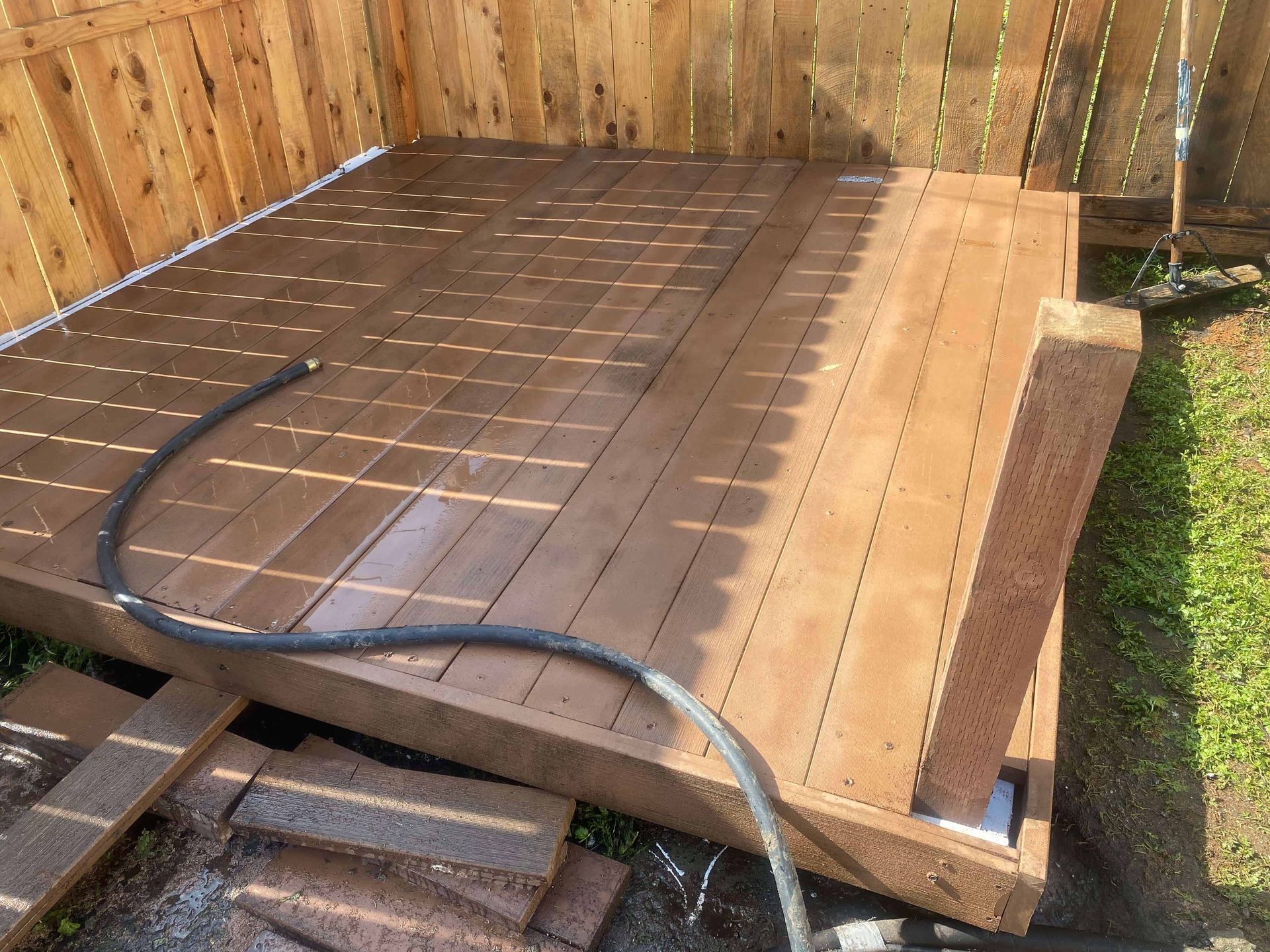 A hose is sitting on a wooden deck next to a wooden fence.