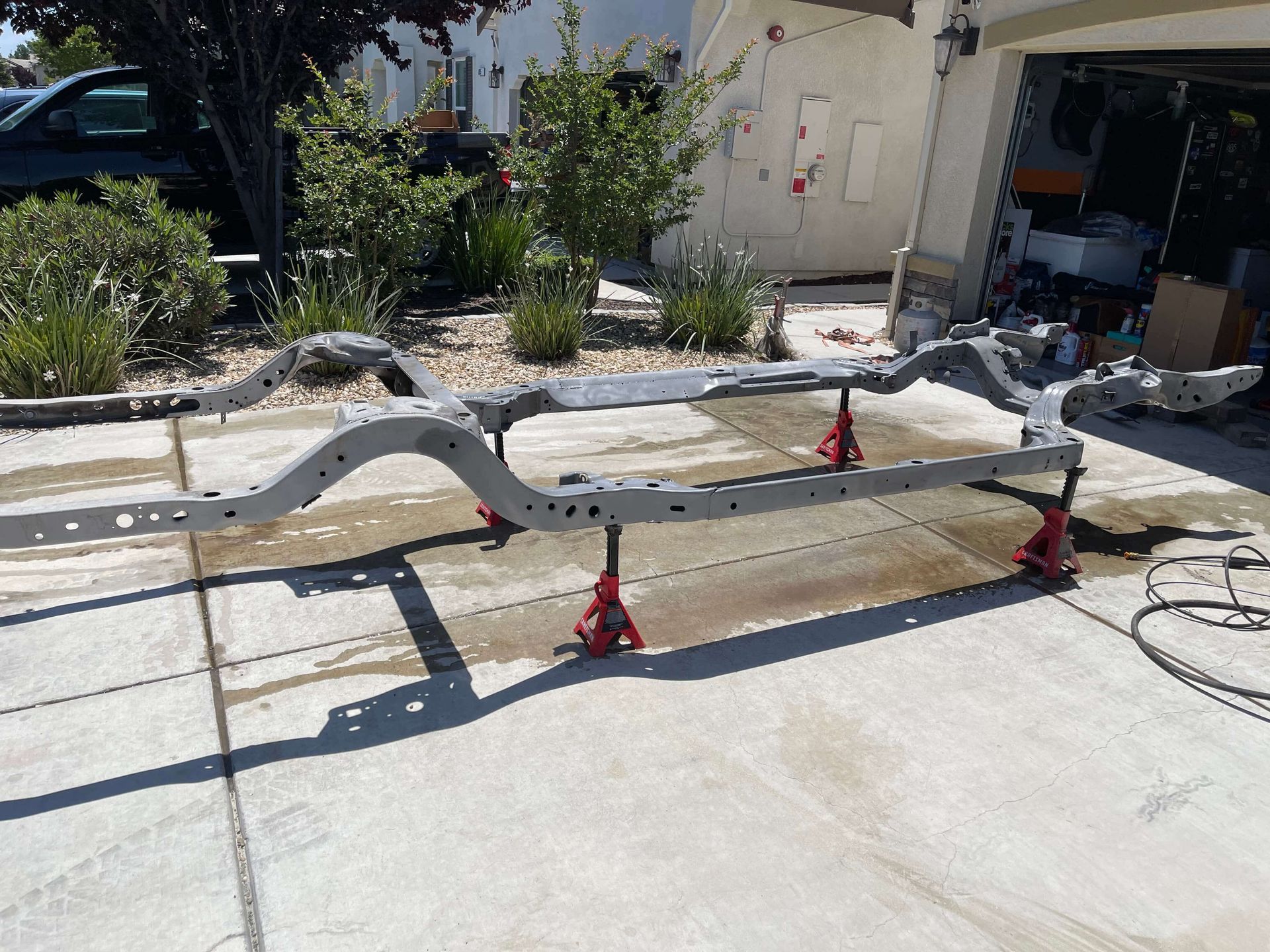 A car frame is sitting on a concrete driveway in front of a garage.