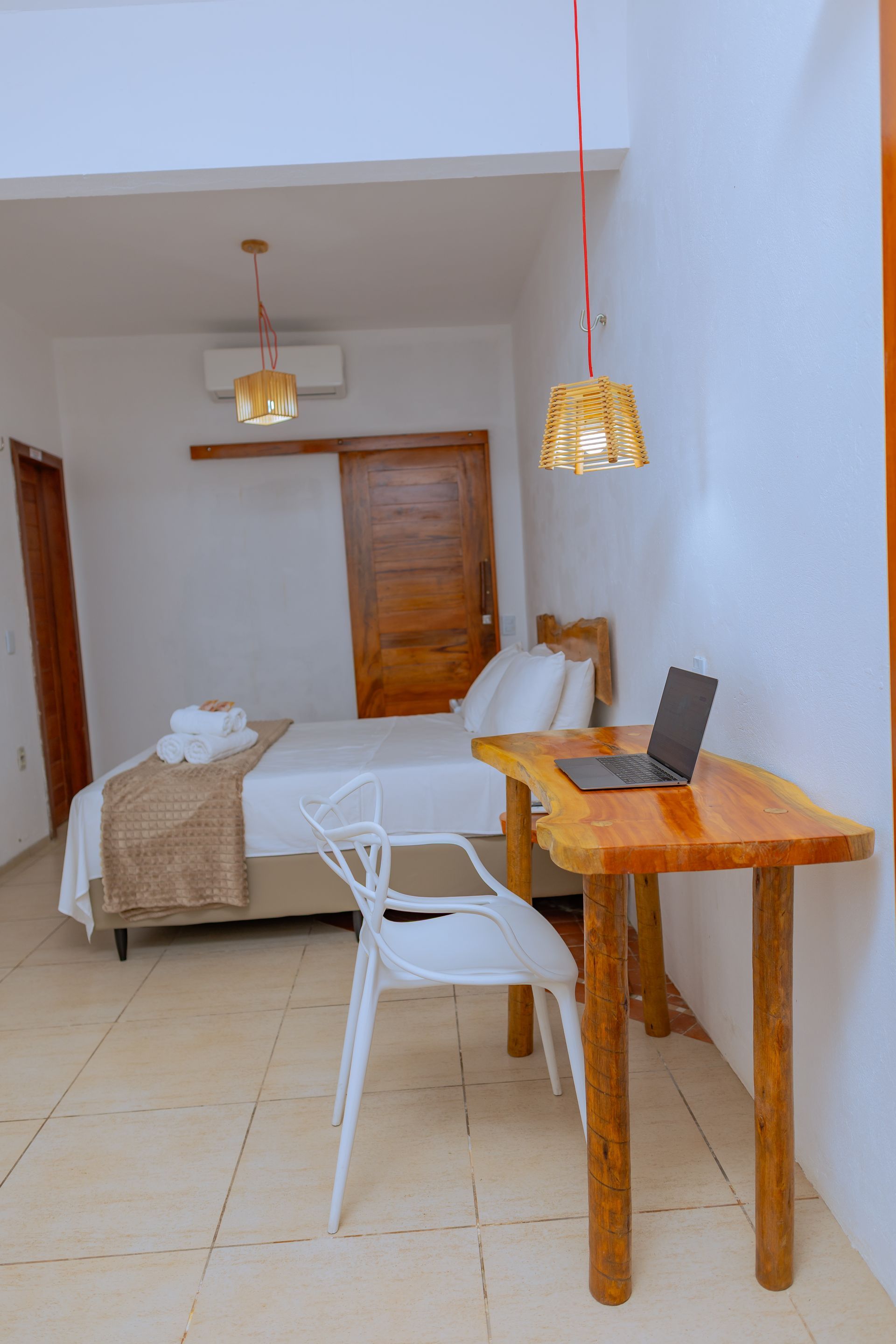 Quarto com cama, escrivaninha de madeira, cadeira branca e laptop.