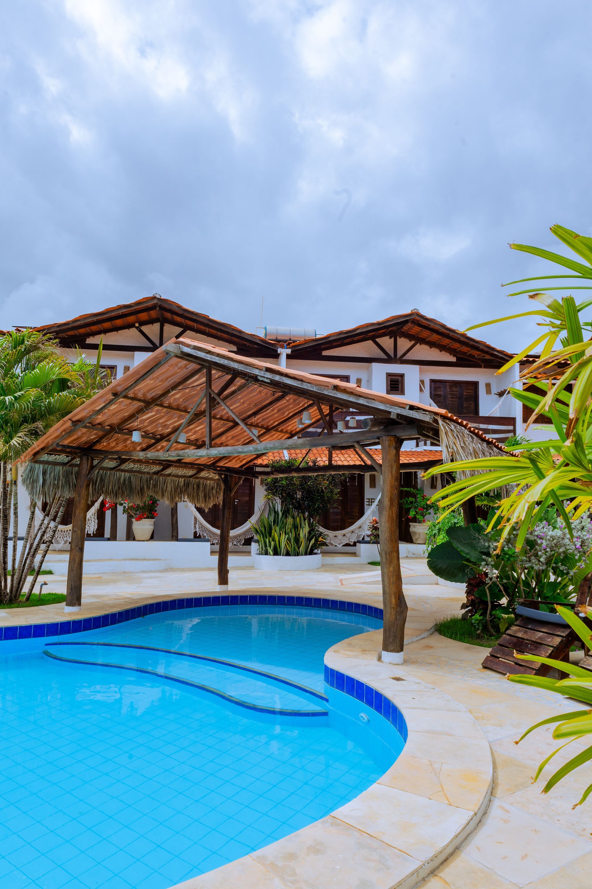Sala aconchegante com teto de madeira, árvore de Natal, poltronas, mesa de jantar e grandes janelas com vista para uma vegetação exuberante.
