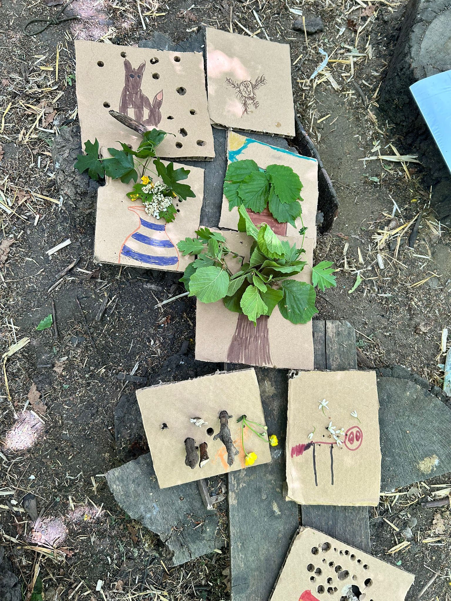 Brown paper art with drawings and plants, arranged on wooden planks.