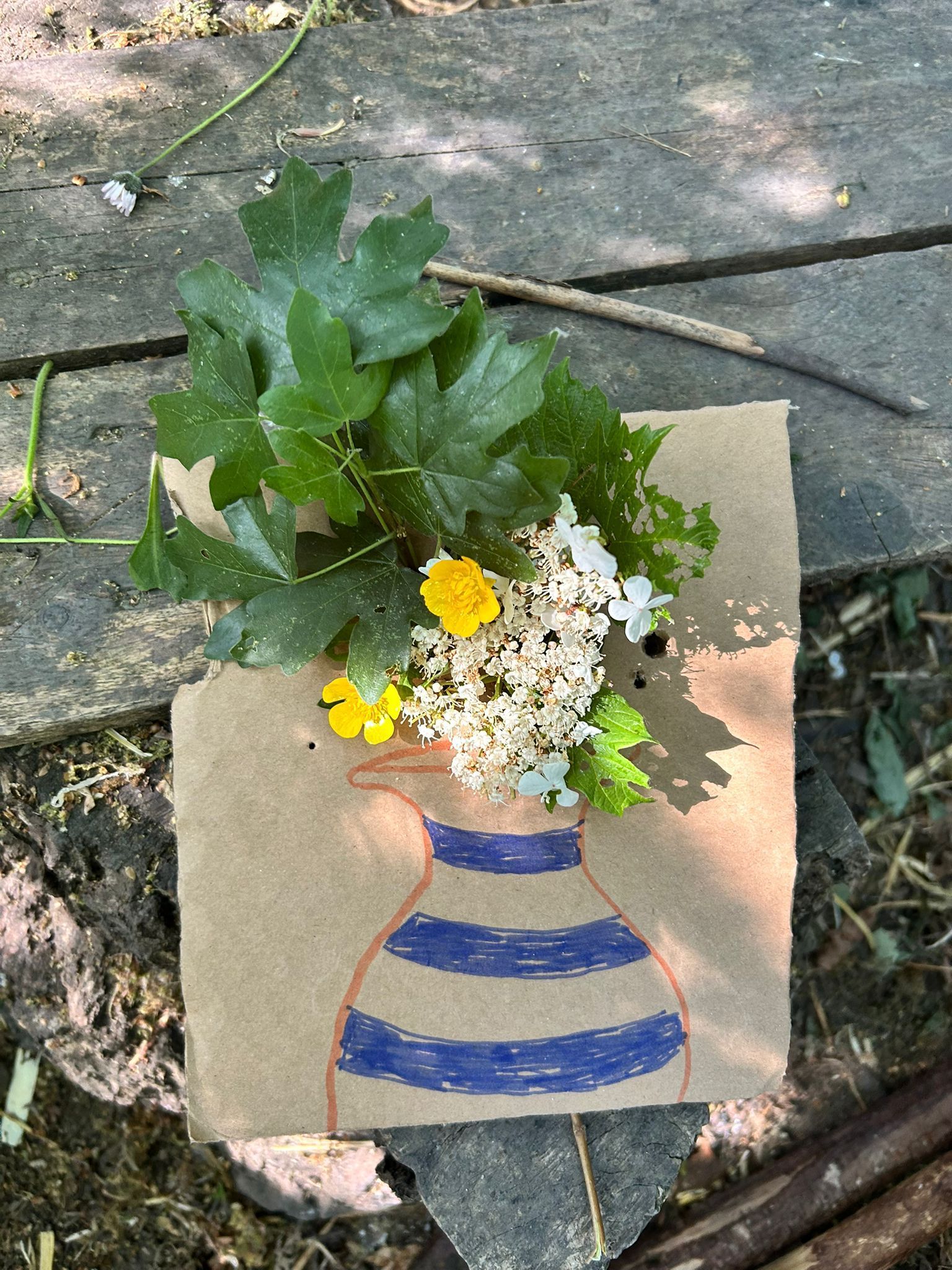 Nature art: leaves and flowers arranged in a vase drawn on brown paper, on a wooden surface.