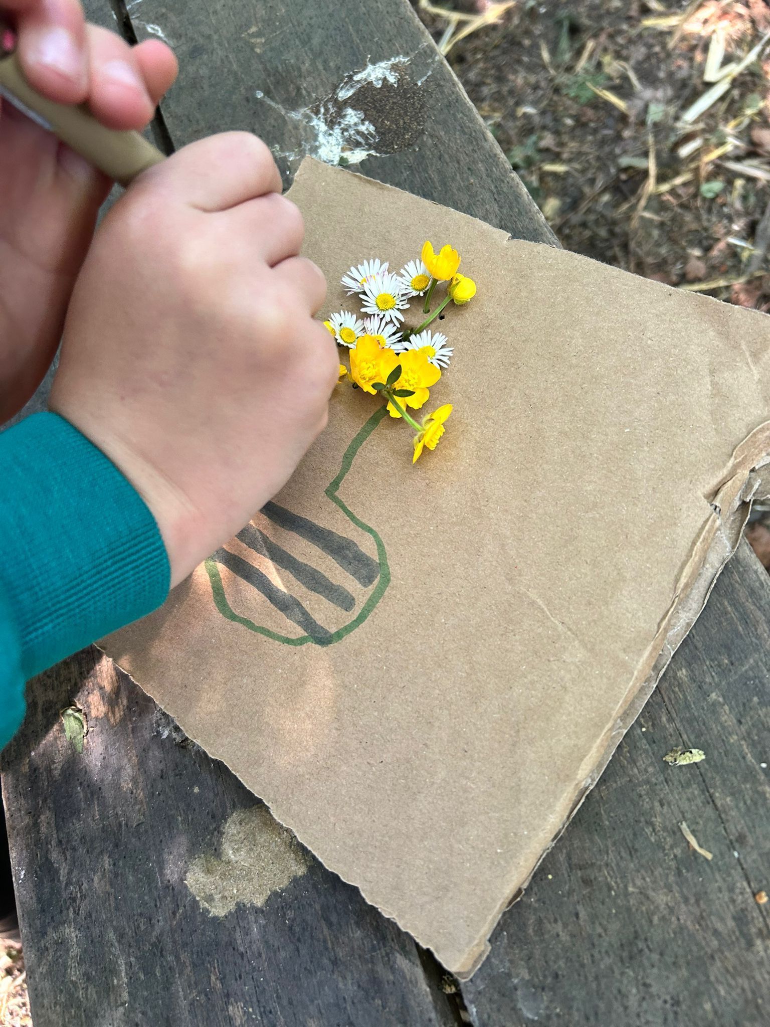 Child pressing yellow flowers onto cardboard art, drawing vase.