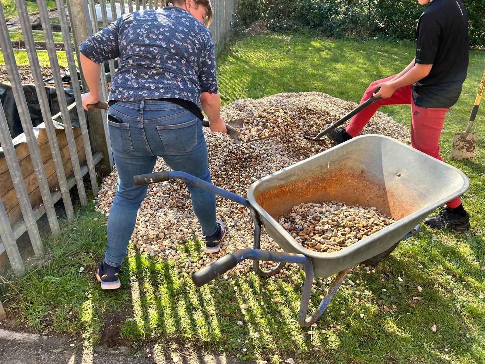 Two people are pushing a wheelbarrow full of mulch.