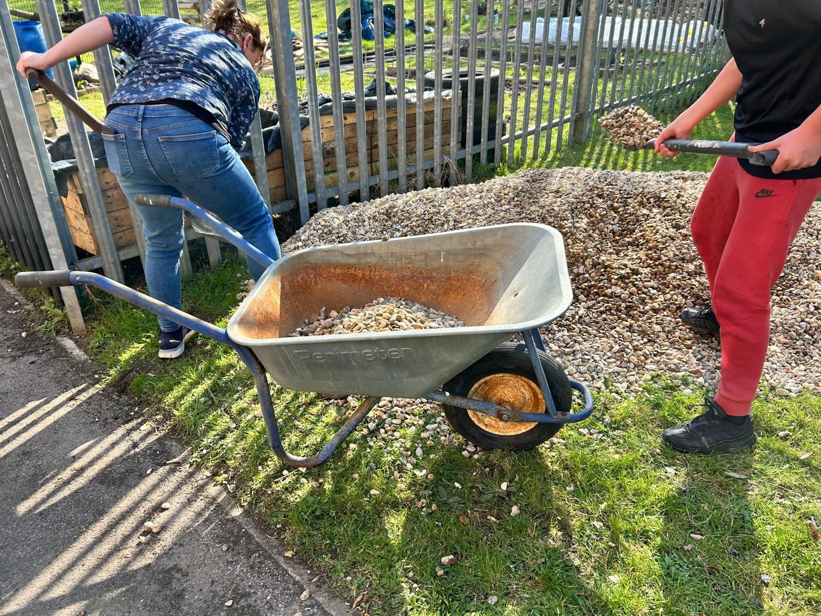 Two people are pushing a wheelbarrow full of dirt.
