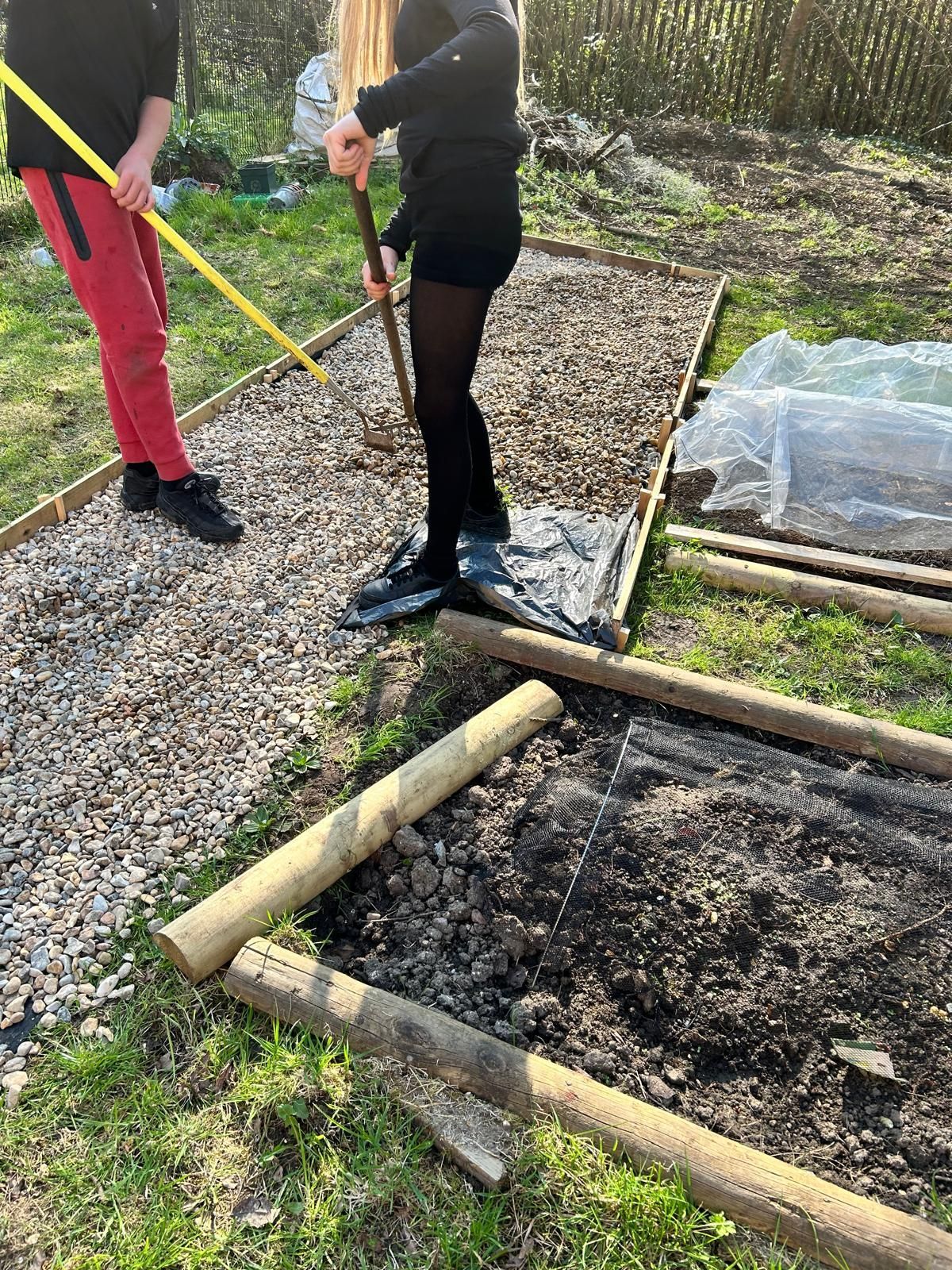 A man and a woman are raking dirt in a garden.