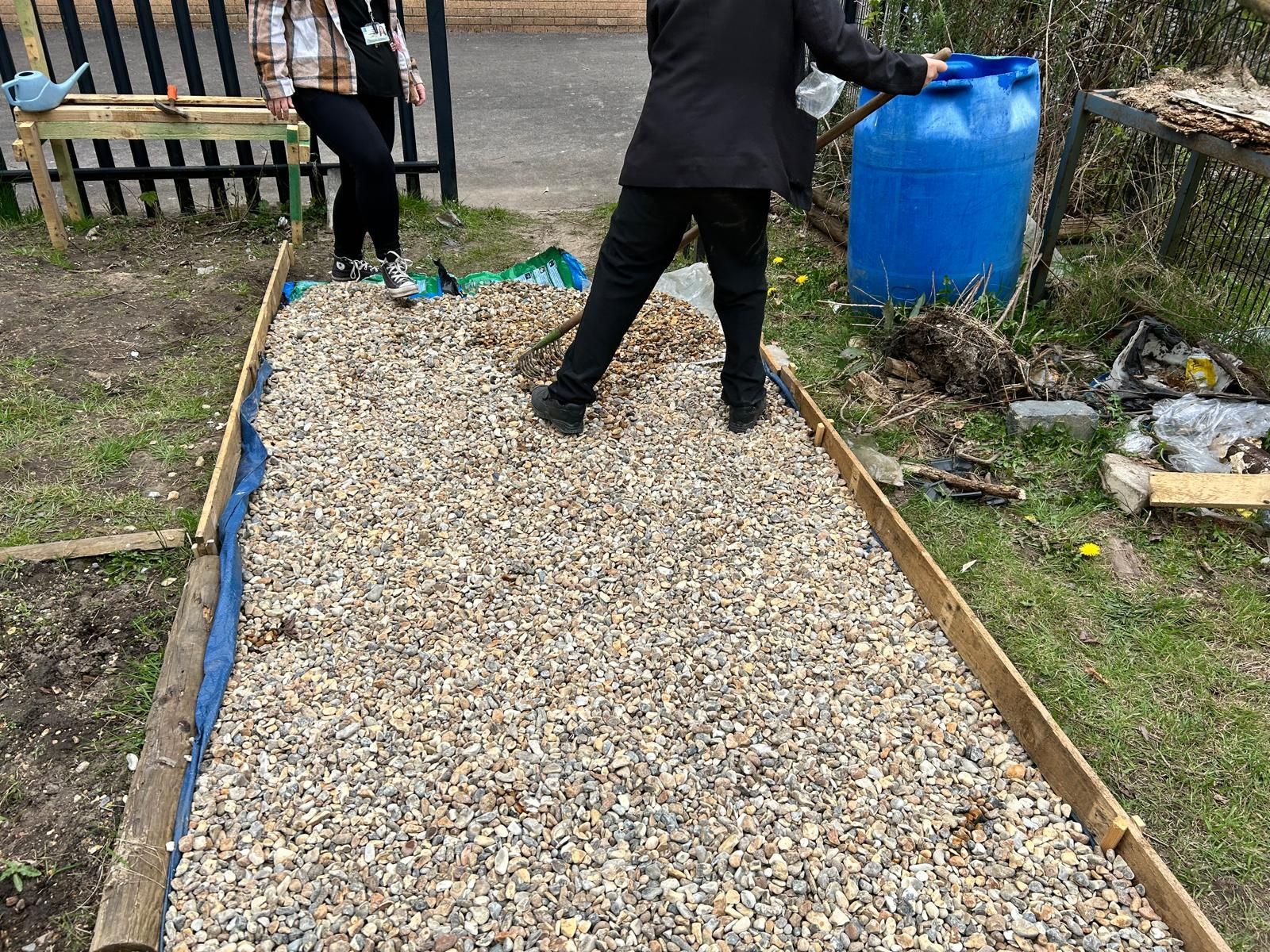 A woman is standing on a pile of gravel next to a blue barrel.