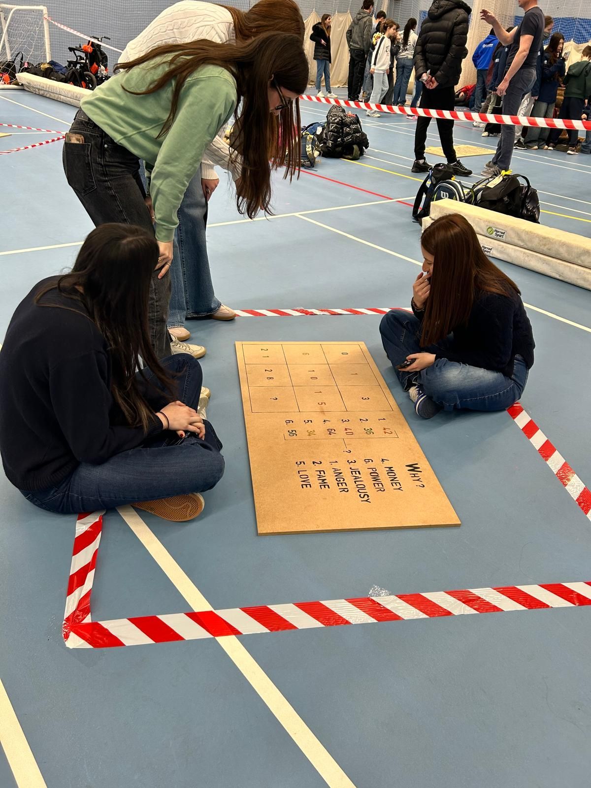 Three teenagers are sitting on the floor looking at a piece of cardboard.