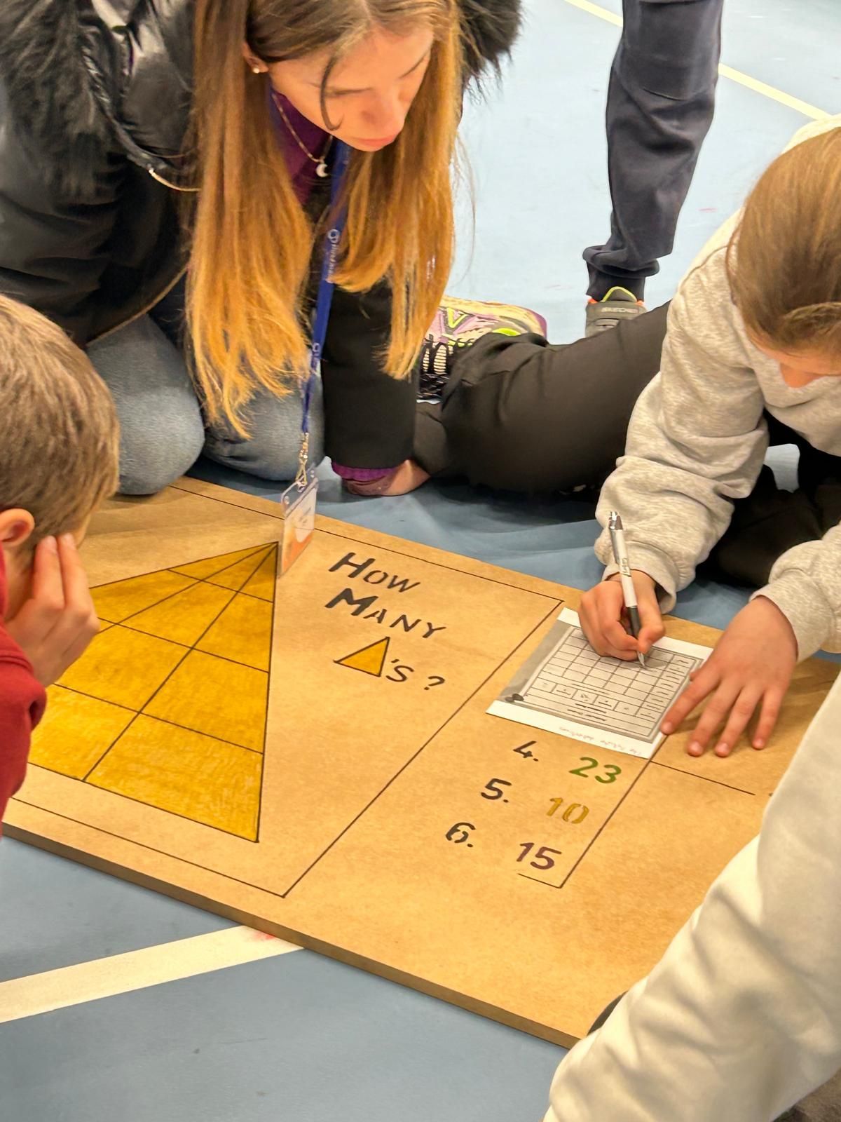 A group of children are sitting on the floor looking at a board with numbers on it.
