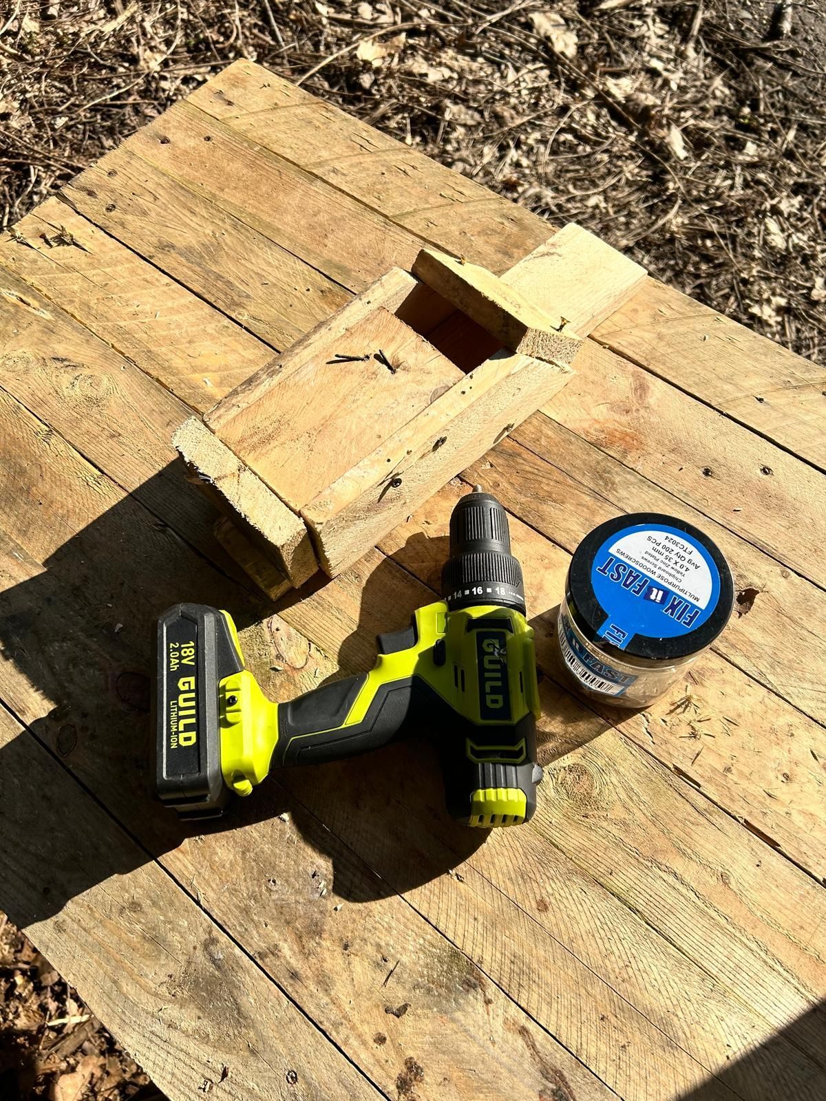 A drill is sitting on top of a wooden table next to a jar of glue.