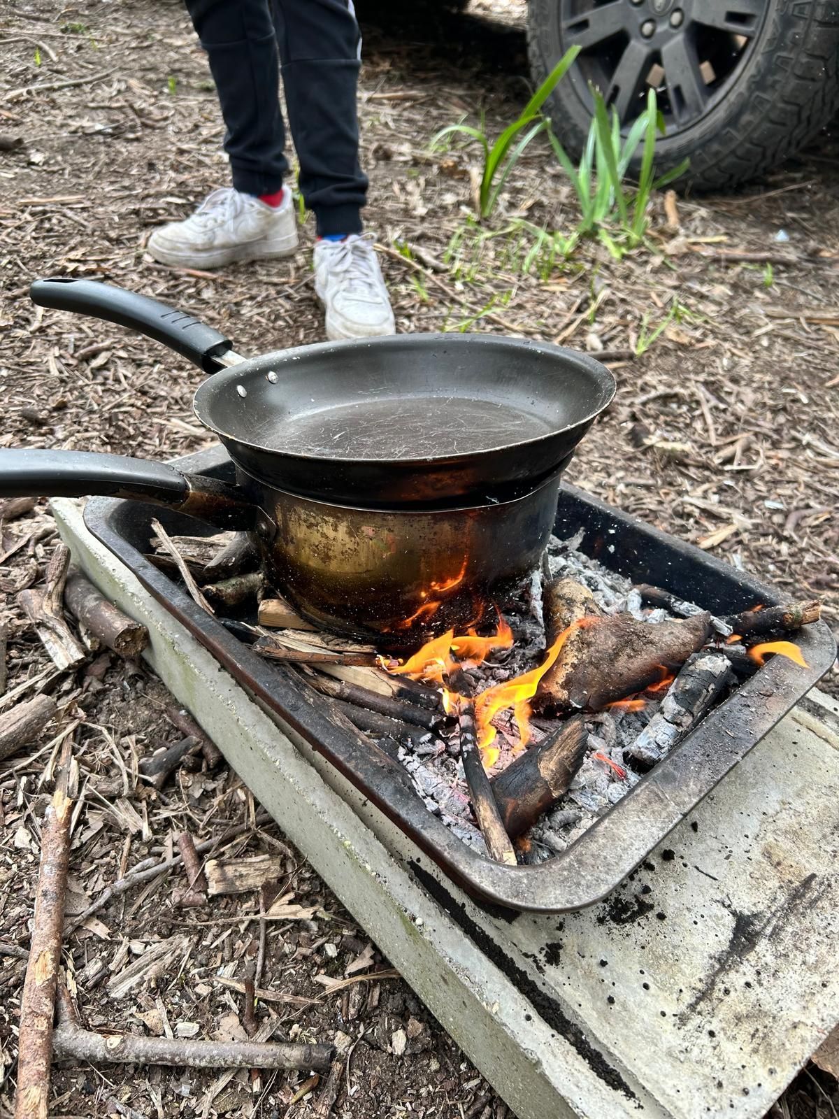 A person is cooking food in a pan over a fire.