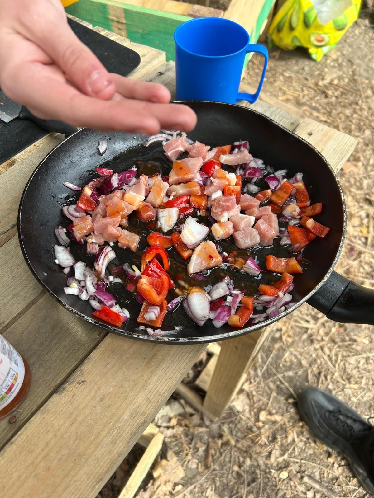 A person is cooking food in a frying pan on a wooden table.