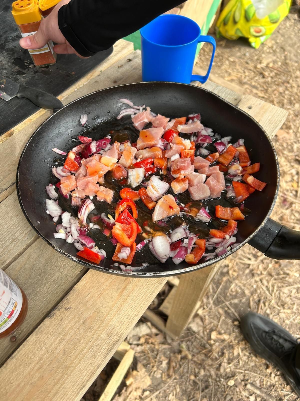 A person is cooking food in a frying pan on a wooden table.