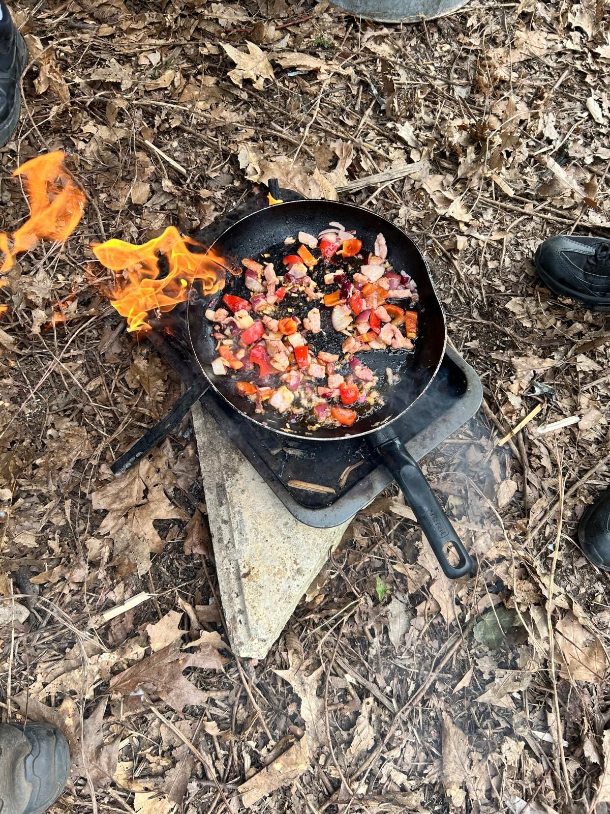A pan of food is cooking on a stove in the woods.