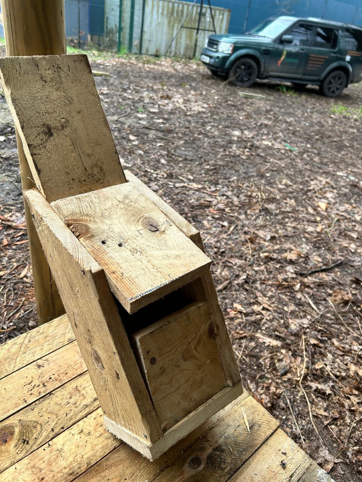 A wooden chair is sitting on a wooden deck next to a car.