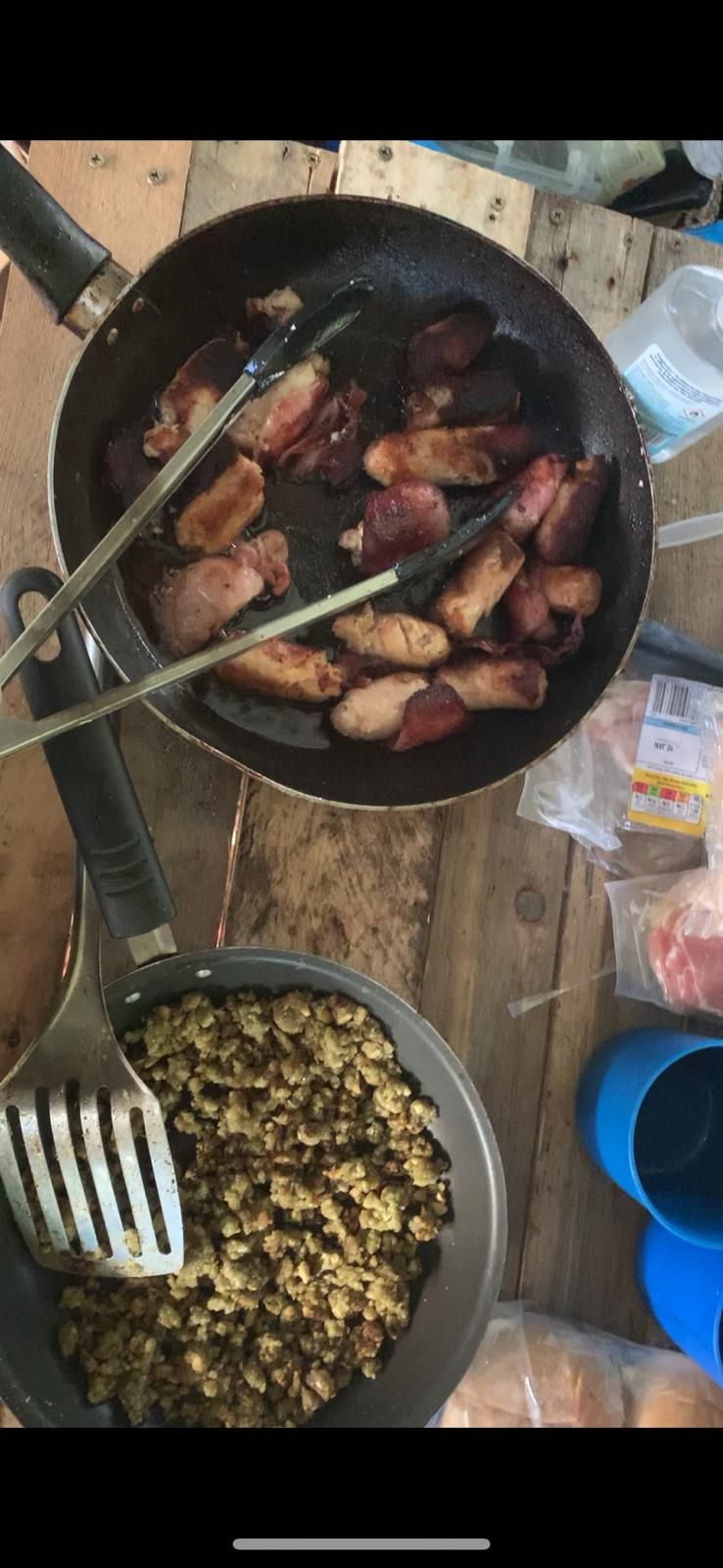 A pan of bacon and sausages  are sitting on a wooden table.