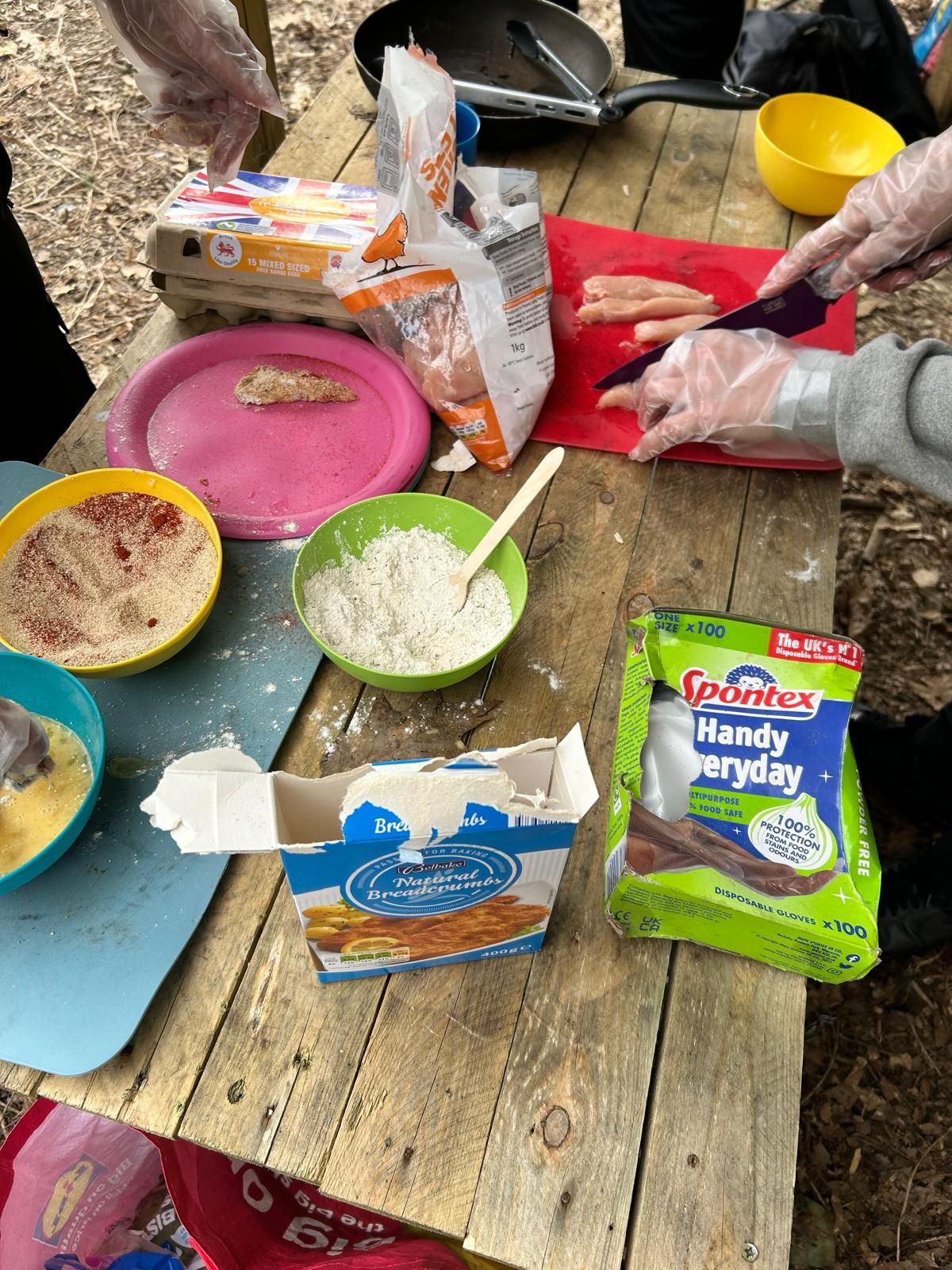 A wooden table topped with bowls of food and a bag of handy gloves.