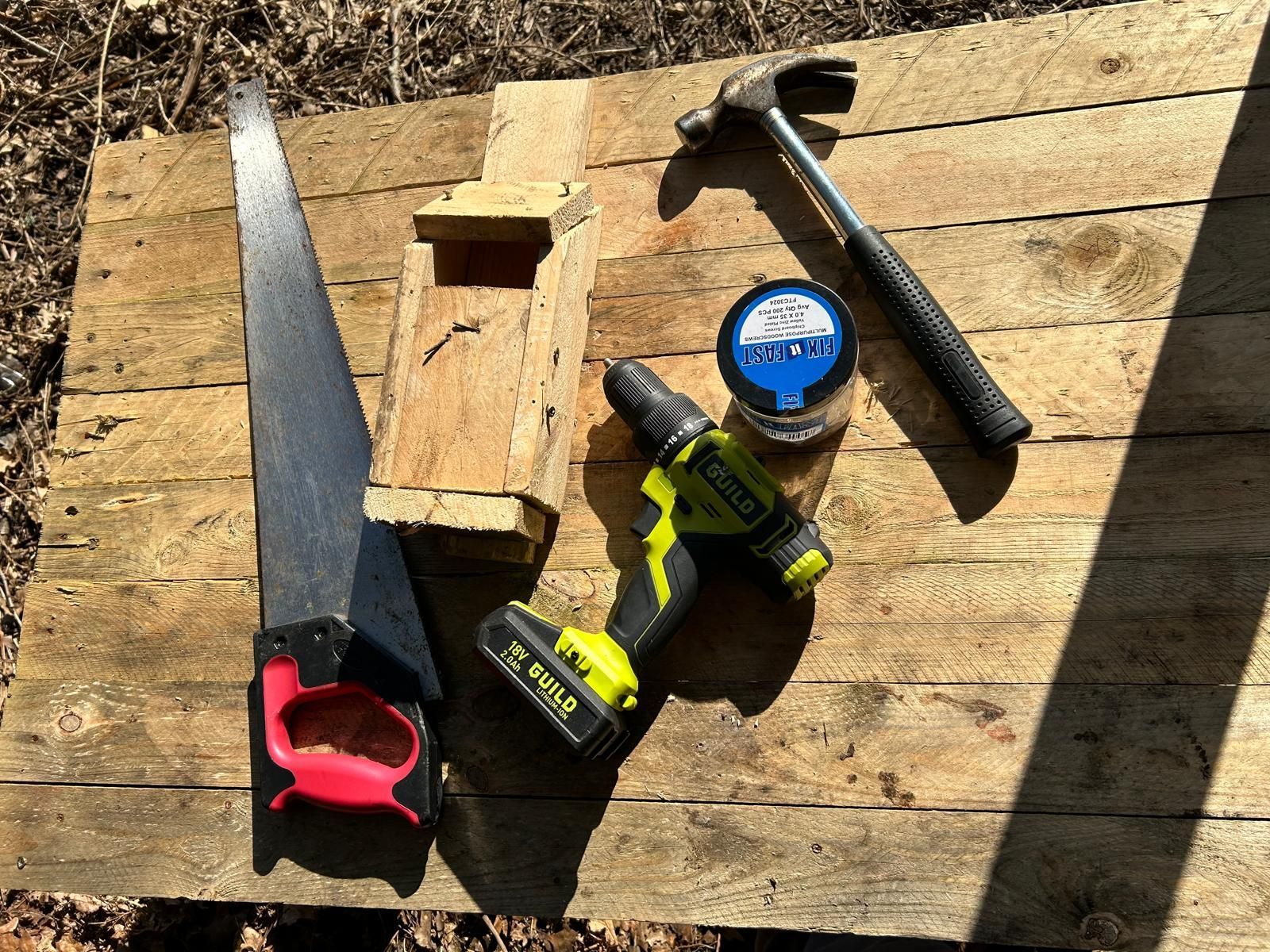 A drill , saw , and hammer are sitting on a wooden table.