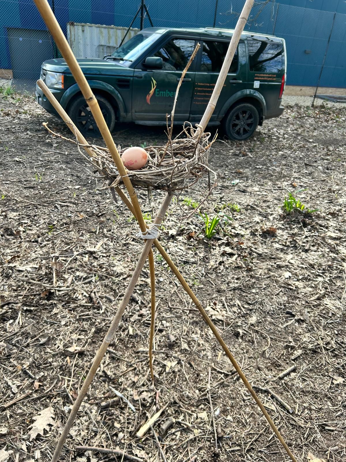 A bird nest with an egg in it is sitting in the dirt in front of a car.