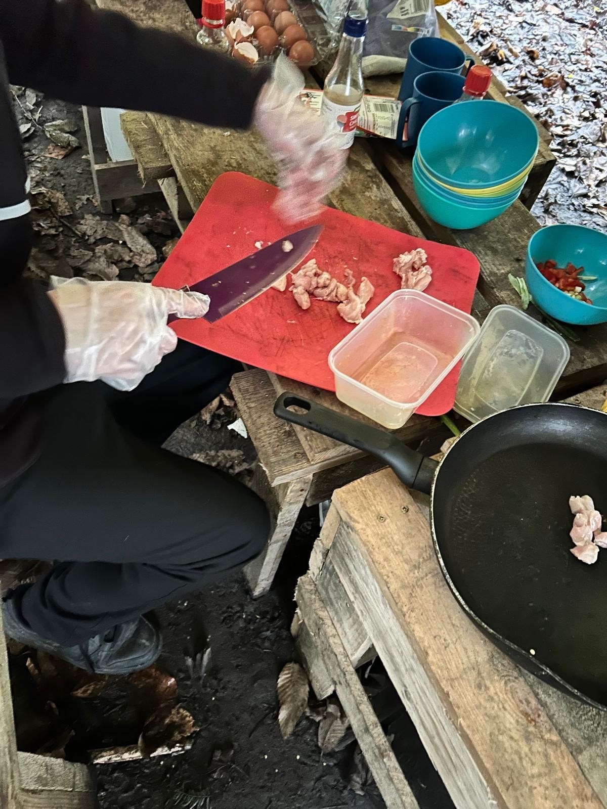 A person is cutting meat on a red cutting board.