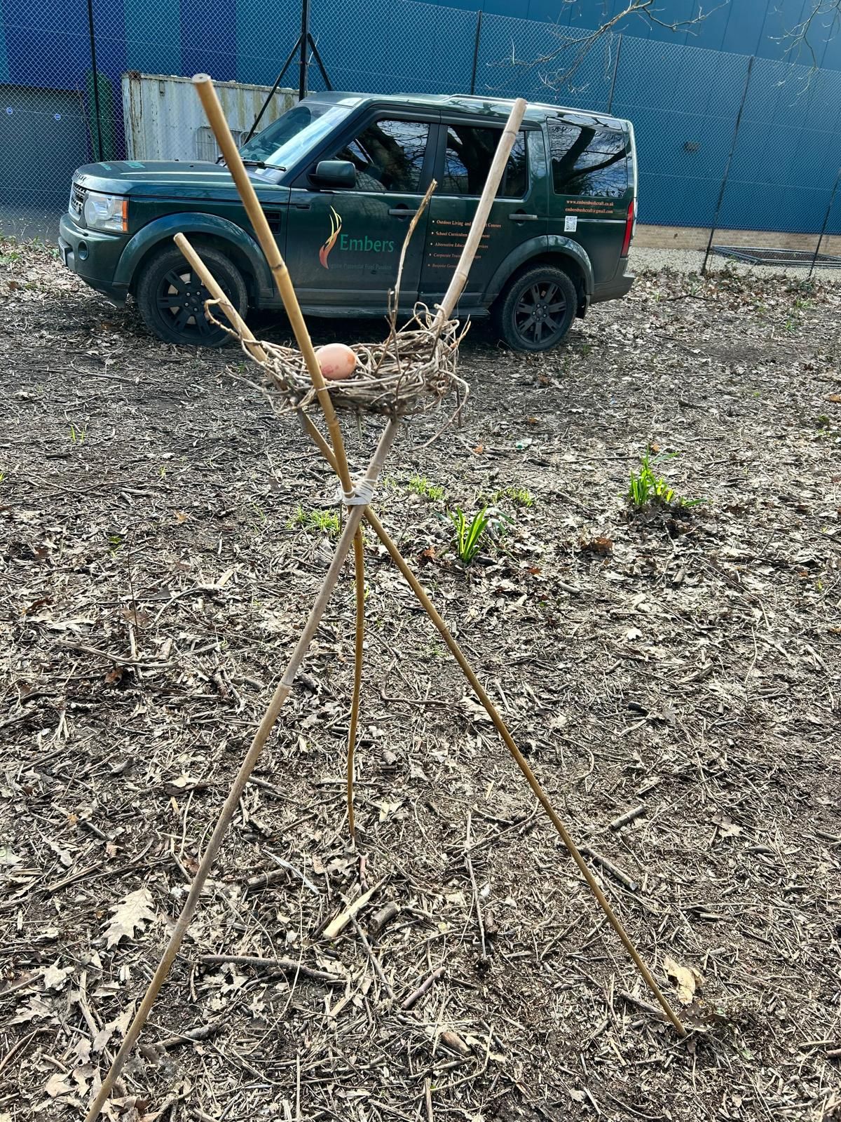 A green suv is parked in a pile of mulch next to a wooden stick.