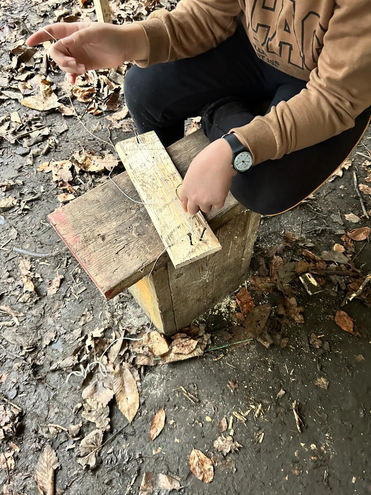 A person is kneeling down on the ground cutting a piece of wood.