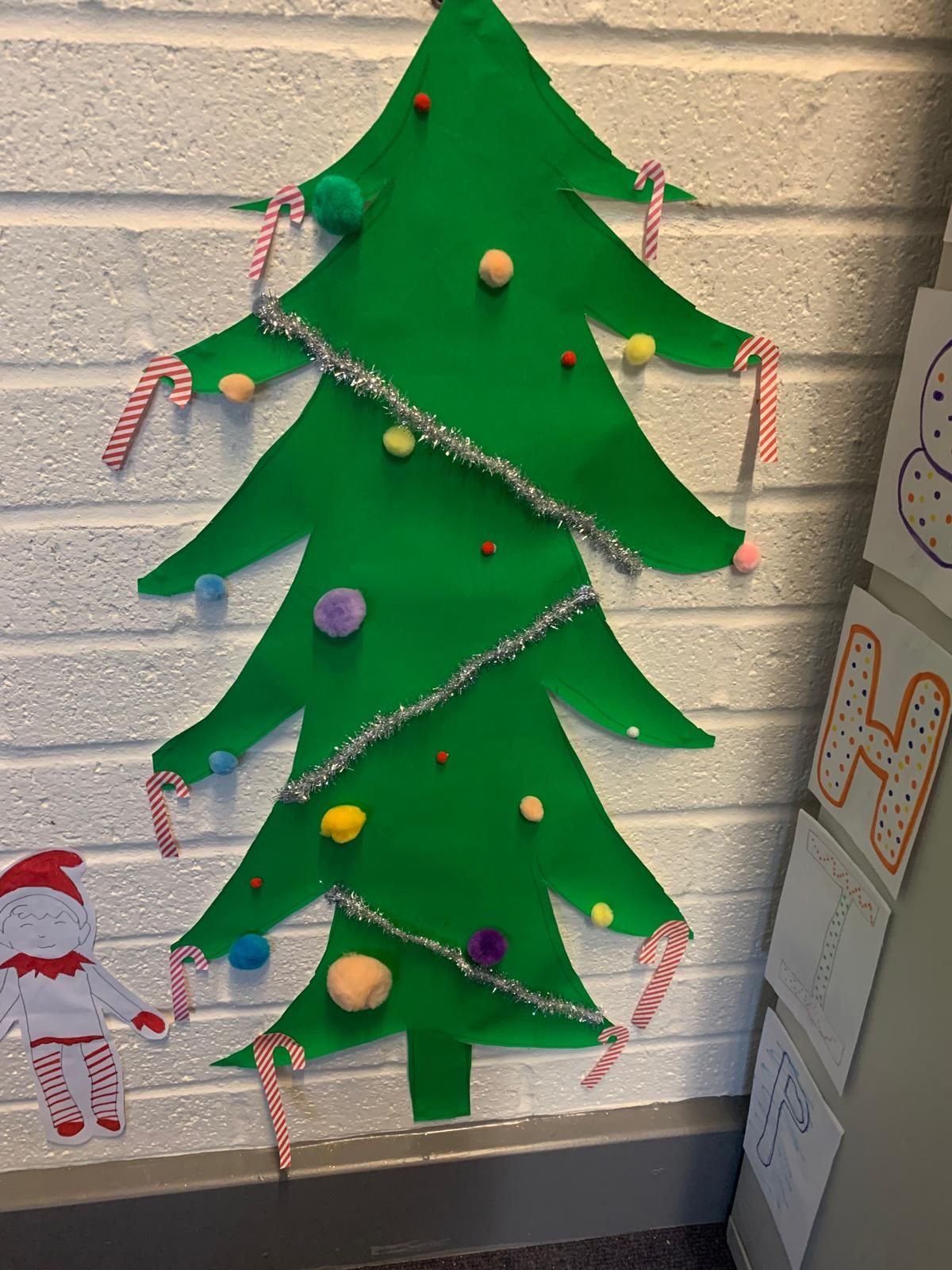 A green christmas tree is hanging on a white brick wall.