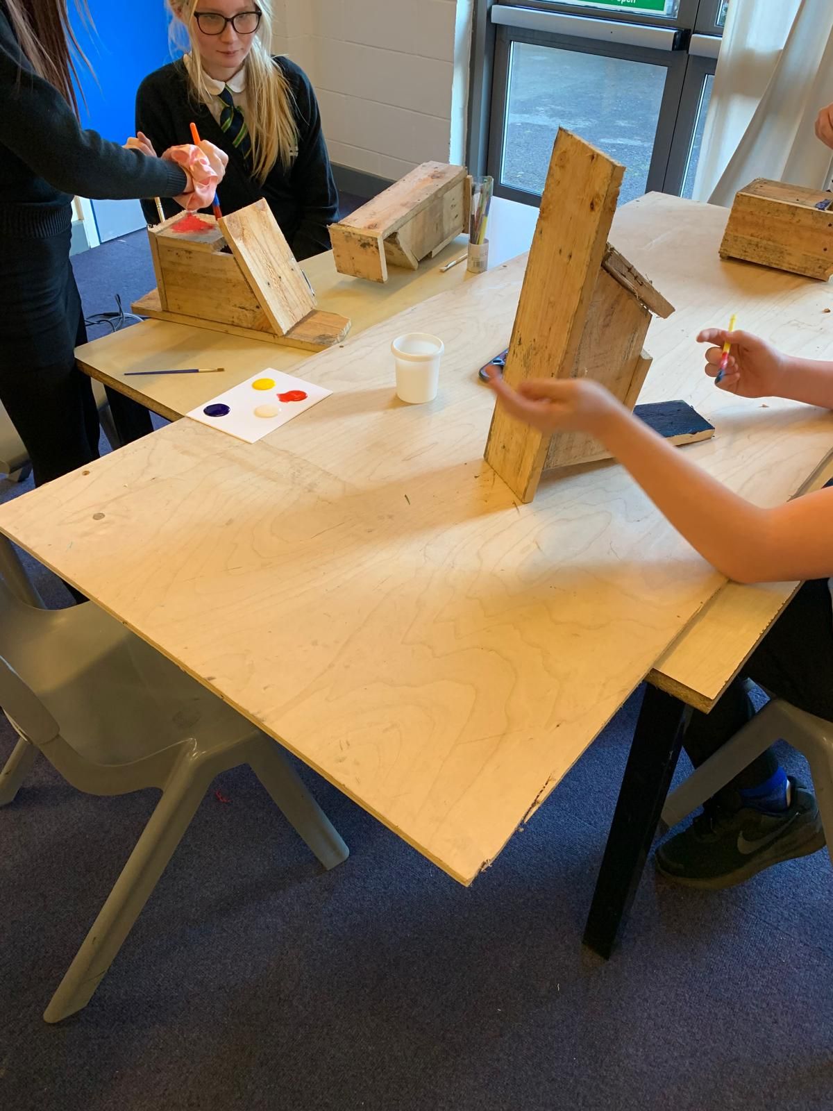 A group of children are sitting at a table making a birdhouse.
