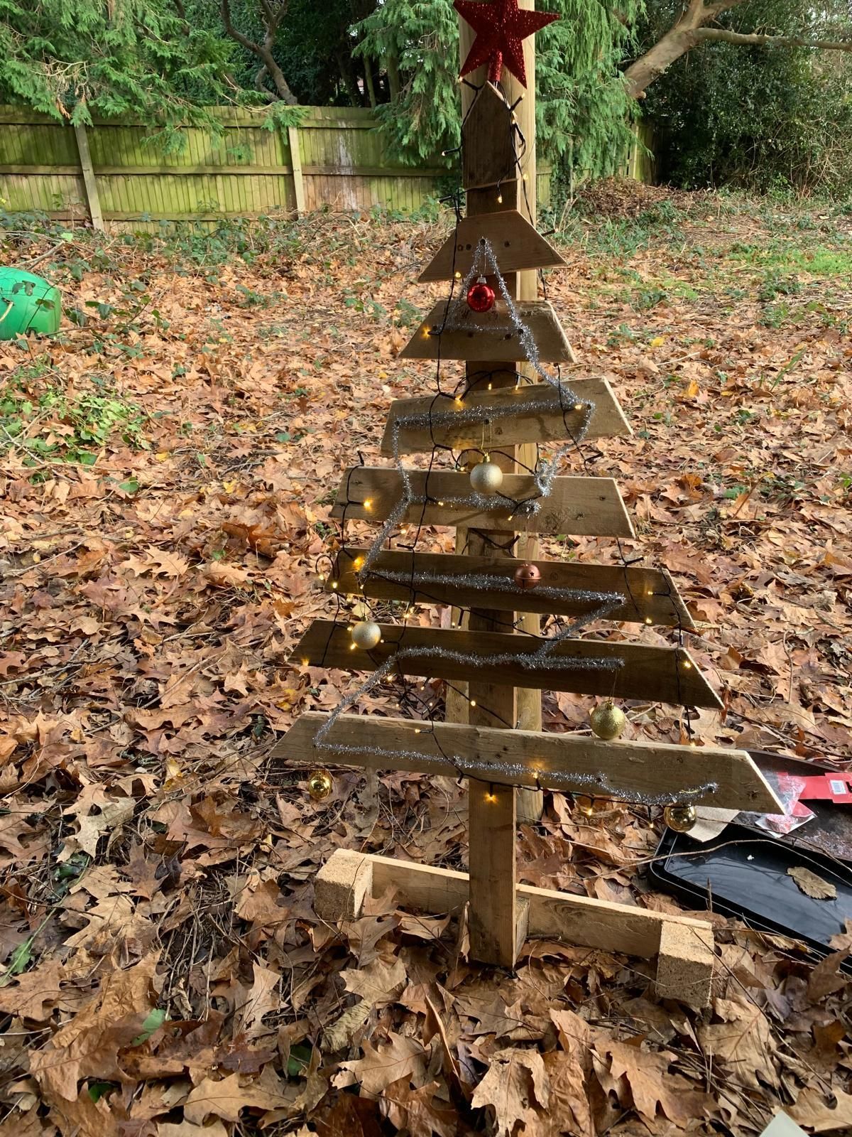 A wooden christmas tree is sitting on top of a pile of leaves.