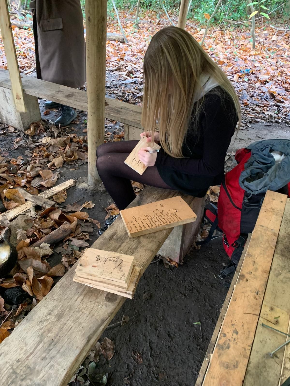 A woman is sitting on a wooden bench in the woods.