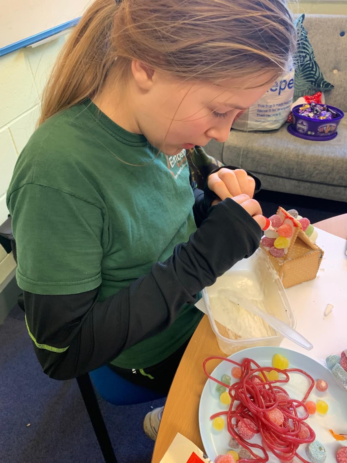A young girl is sitting at a table making a gingerbread house.