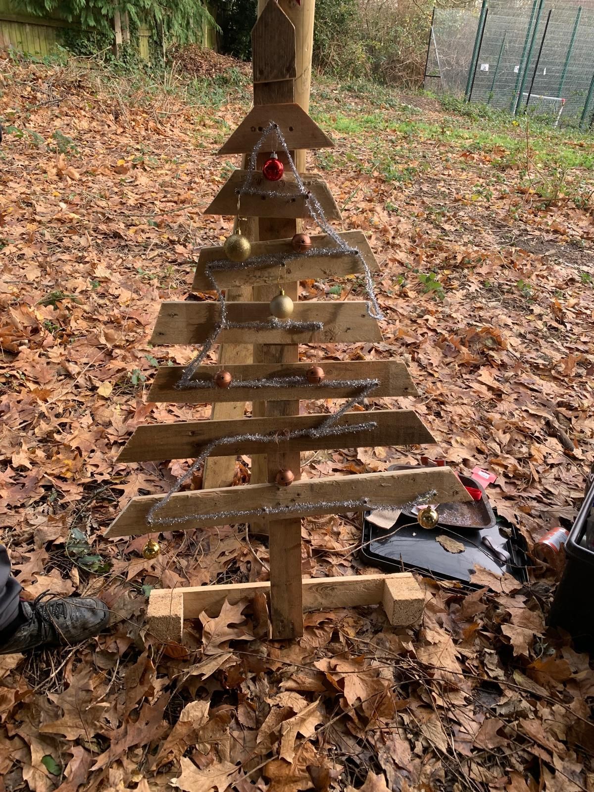 A wooden christmas tree is sitting on top of a pile of leaves.