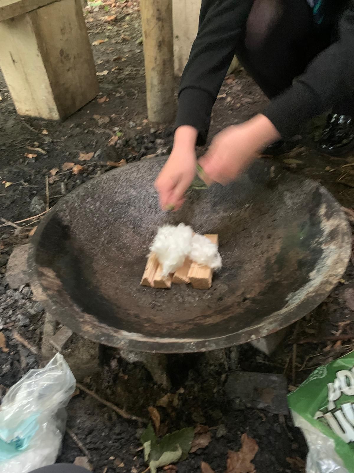 A young person is making a fire in a large bowl.