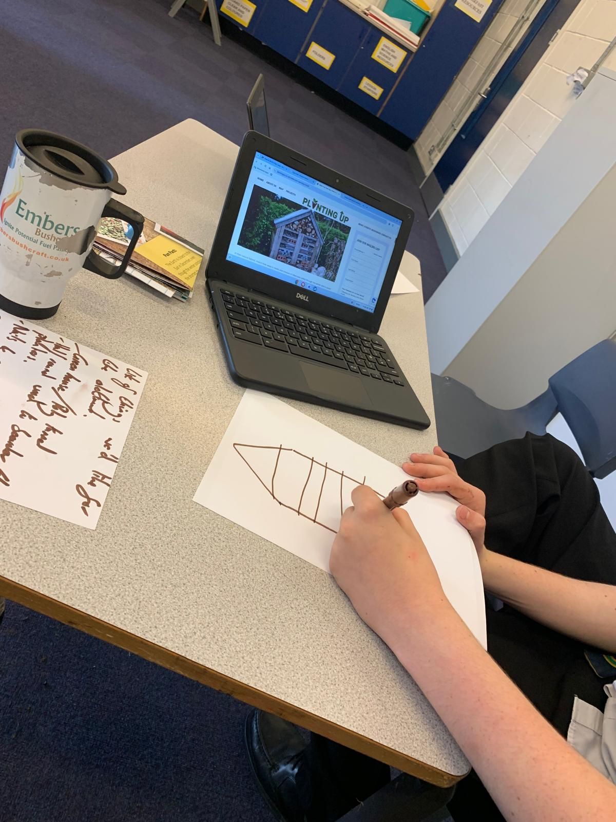 A child is drawing on a piece of paper in front of a laptop computer.