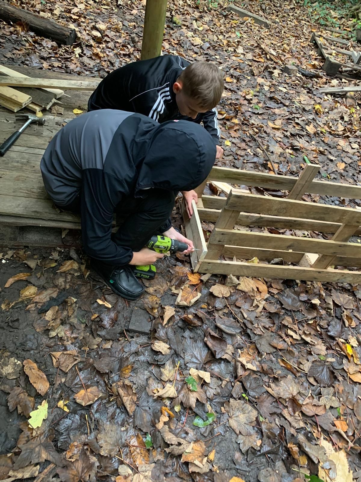 Two young people are working on a wooden pallet in the woods.
