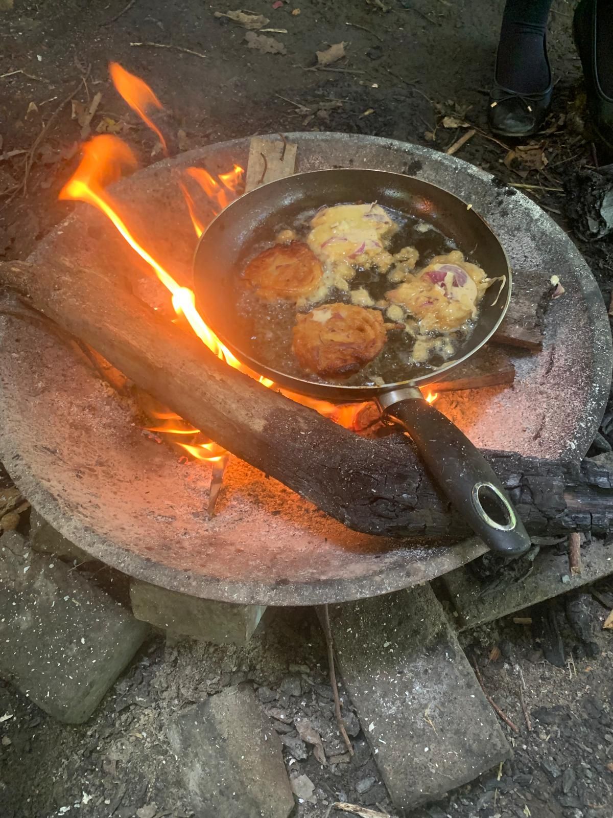 A pan of food is cooking on a fire pit.