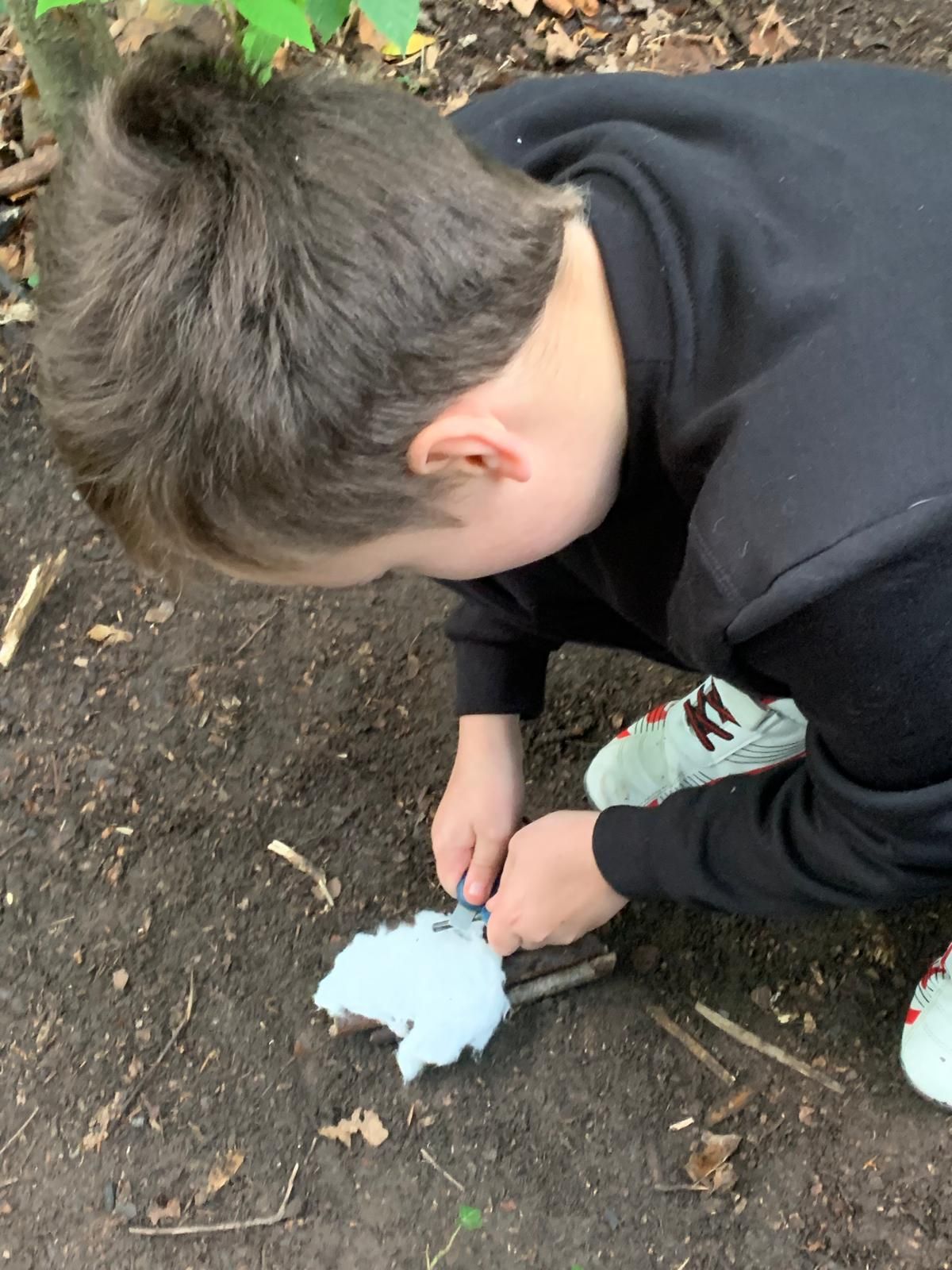 A young boy is kneeling down in the dirt holding a tool.