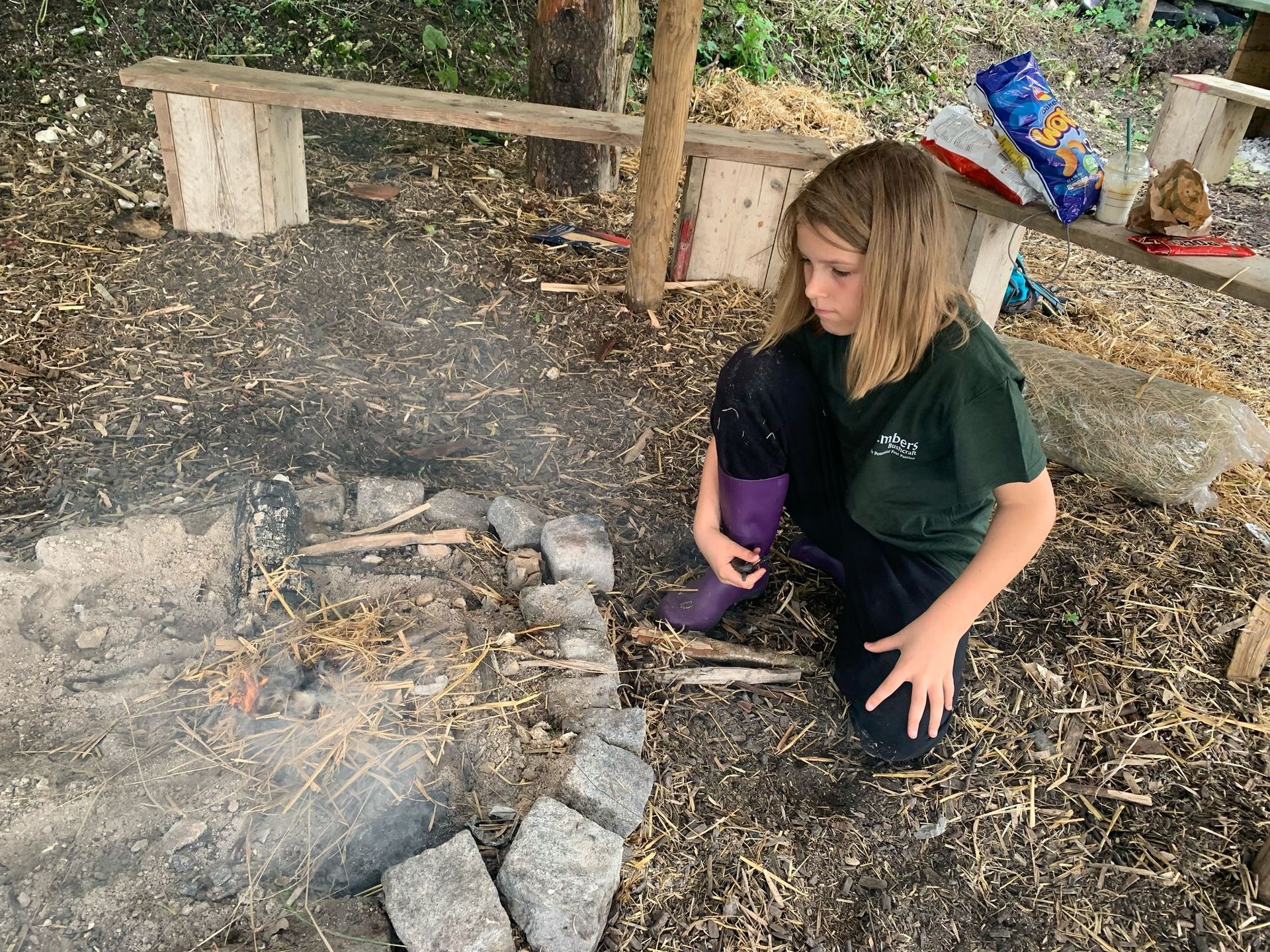 A young girl is sitting on the ground next to a fire pit.