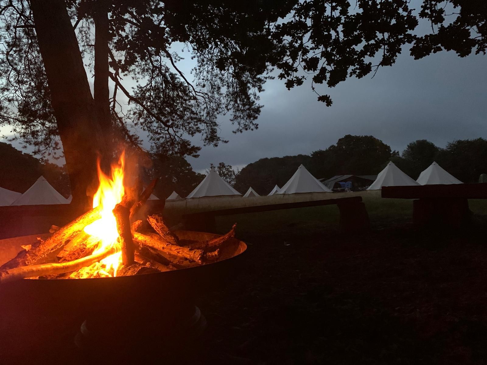 Campfire burning brightly at dusk; tents in background.