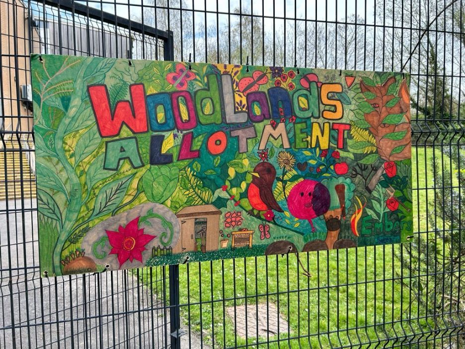 A colorful sign on a fence that says `` woodlands allotment ''.