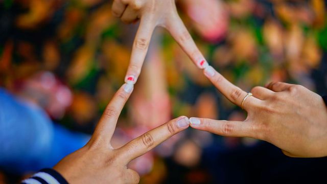 Three hands form a triangle shape with fingers, suggesting teamwork or unity against a blurred background.