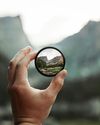 A person is holding a round object with a reflection of a mountain in it.