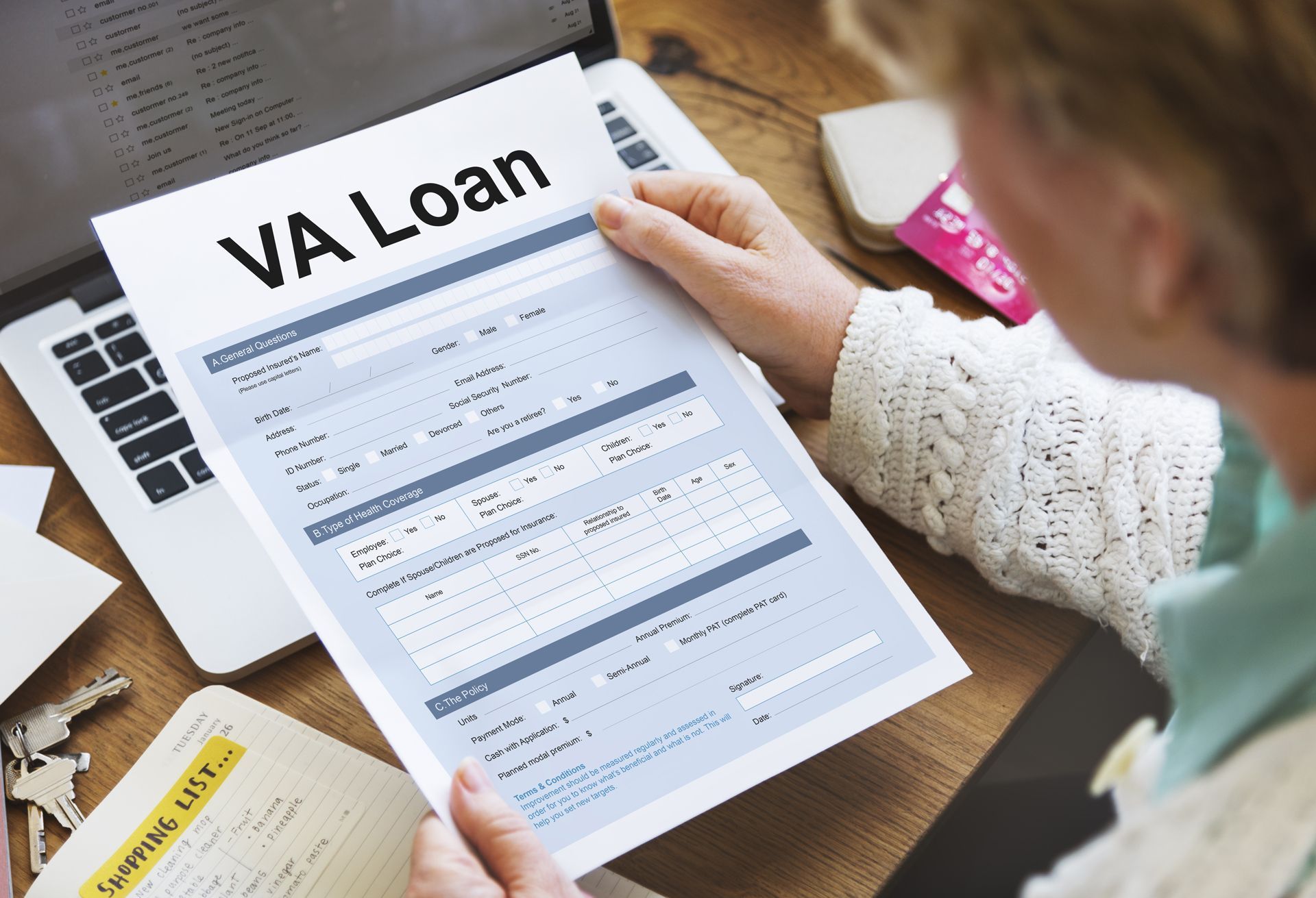 Person examining a VA Loan document at a desk with a laptop and notebook