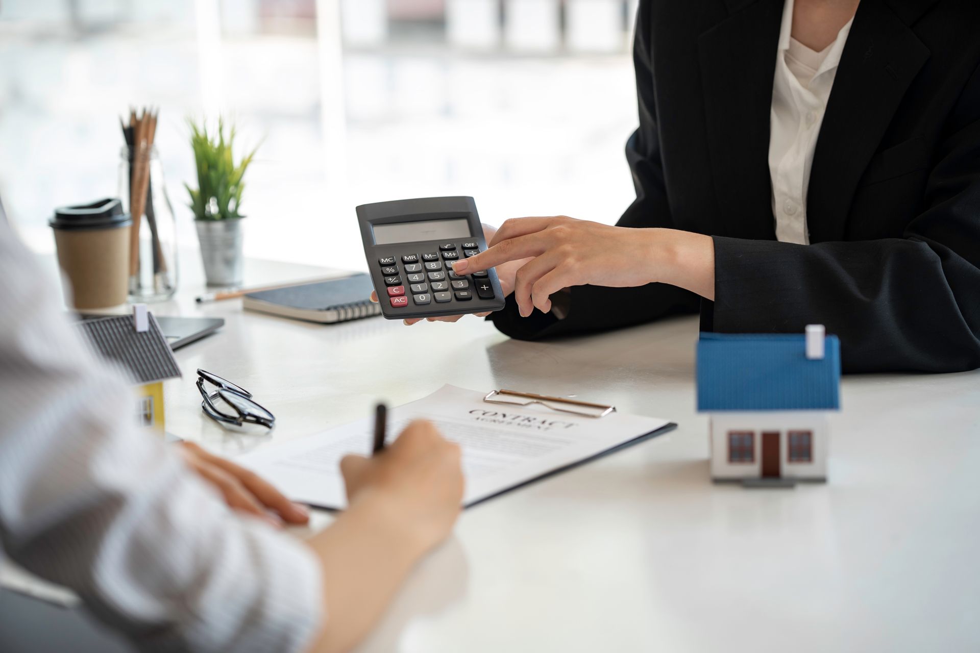 Woman using a calculator, showing figures to a person signing a document, with a model house