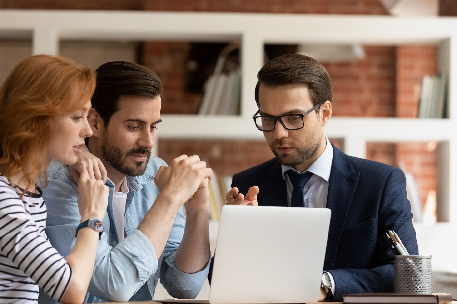 Couple and advisor reviewing information on a laptop, discussing finances in an office setting
