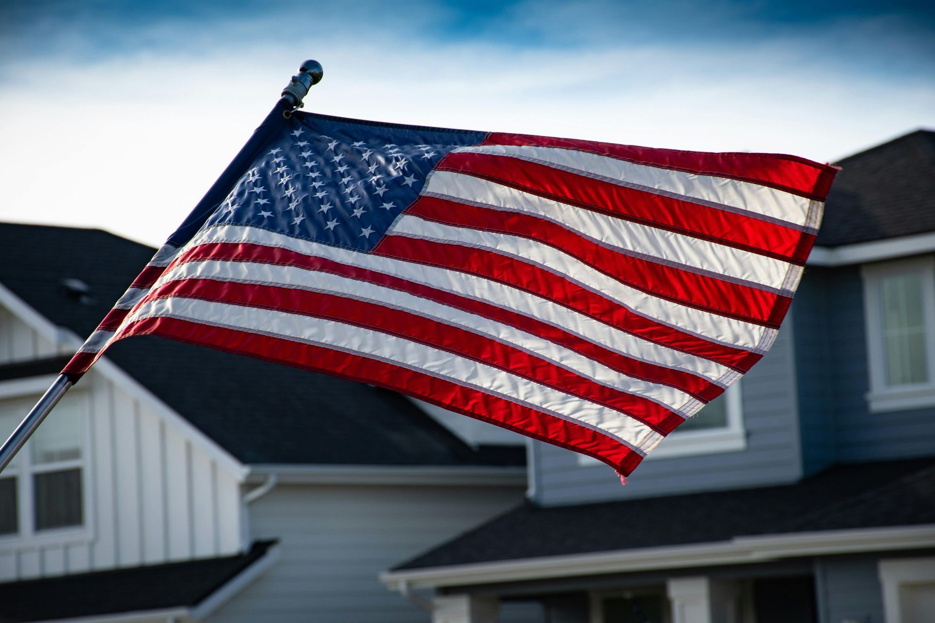American flag waving in front of a residential house on a sunny day