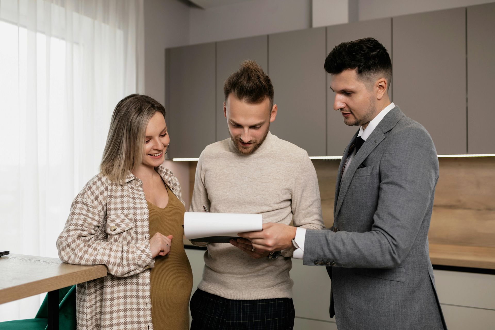 A real estate agent showing paperwork to a smiling couple in a modern kitchen