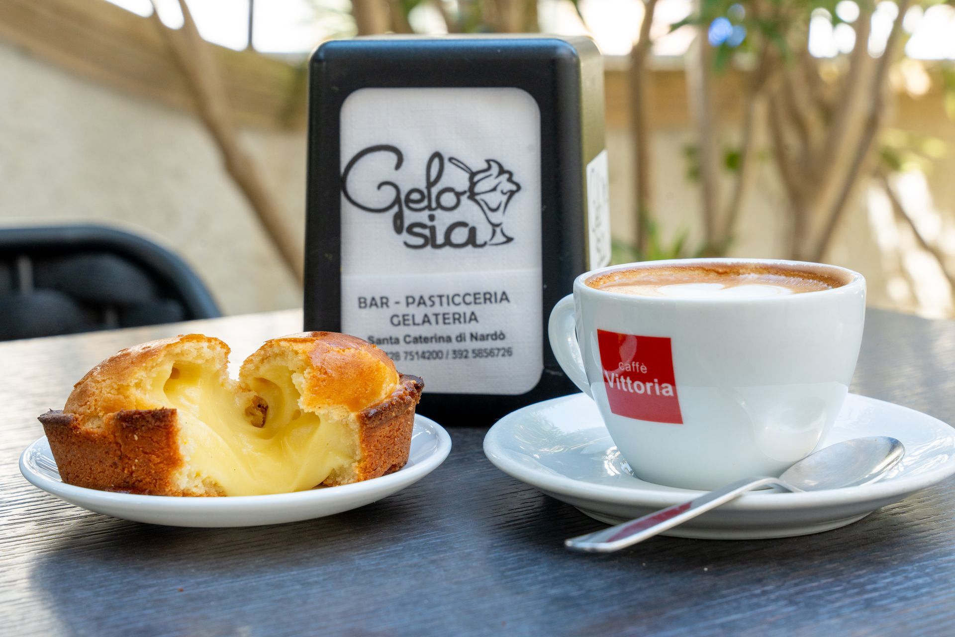Pasticcini e caffè espresso su un tavolino da bar accanto a un'insegna nera di Gelato Signa.