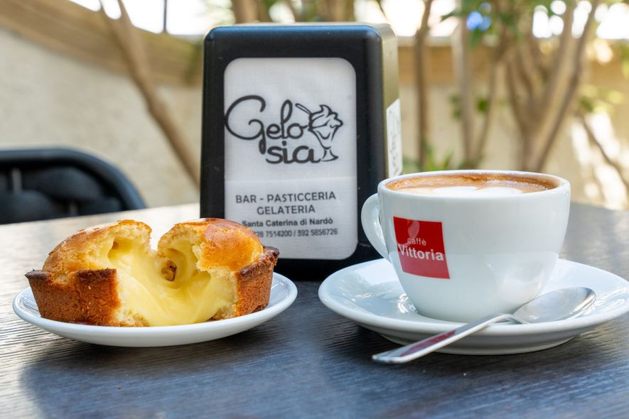 Pasticcini e caffè espresso su un tavolino da bar accanto a un'insegna nera di Gelato Signa.