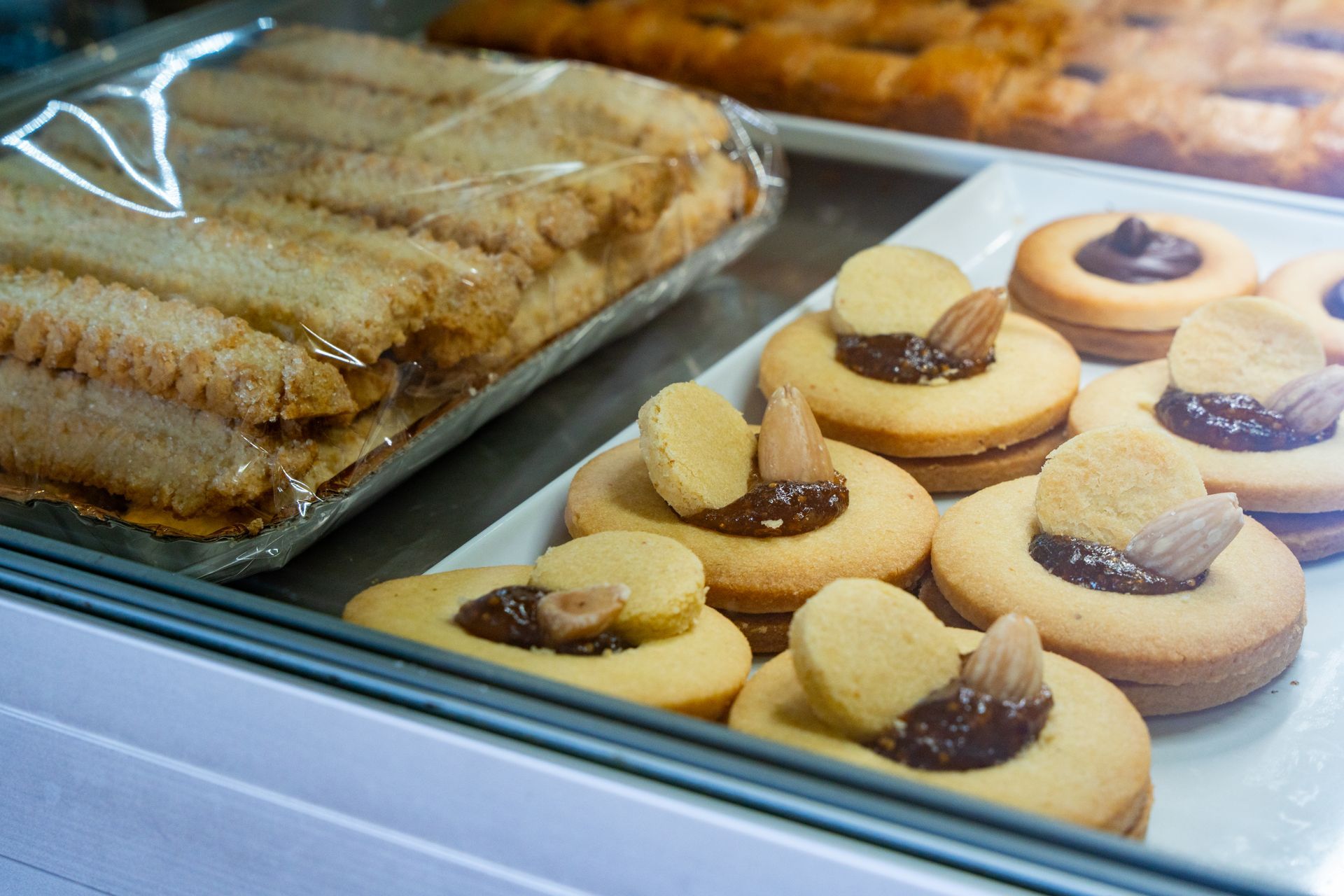 Pasticcini e biscotti in una vetrina di una pasticceria, tra cui panini e biscotti di pasta frolla ripieni di marmellata.